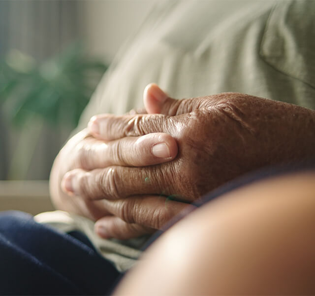 Close-up of an older adult’s hands resting gently together, suggesting calm and mindful breathing.