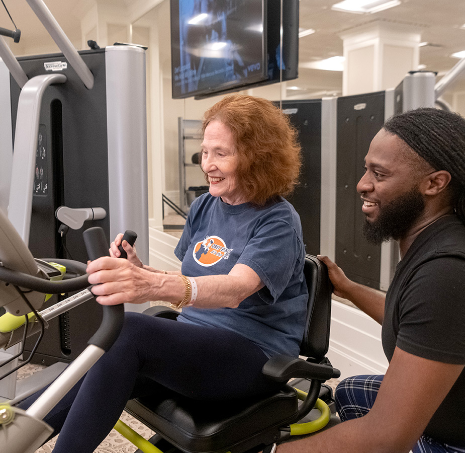 An associate helps a resident use a fitness machine.