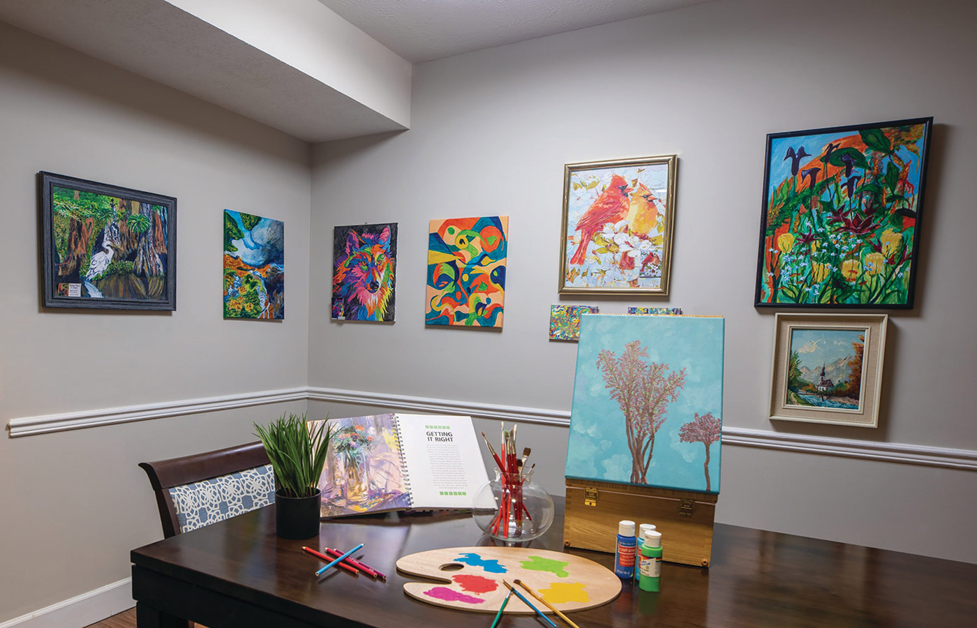 A table with art on top surrounded by paintings on the wall.