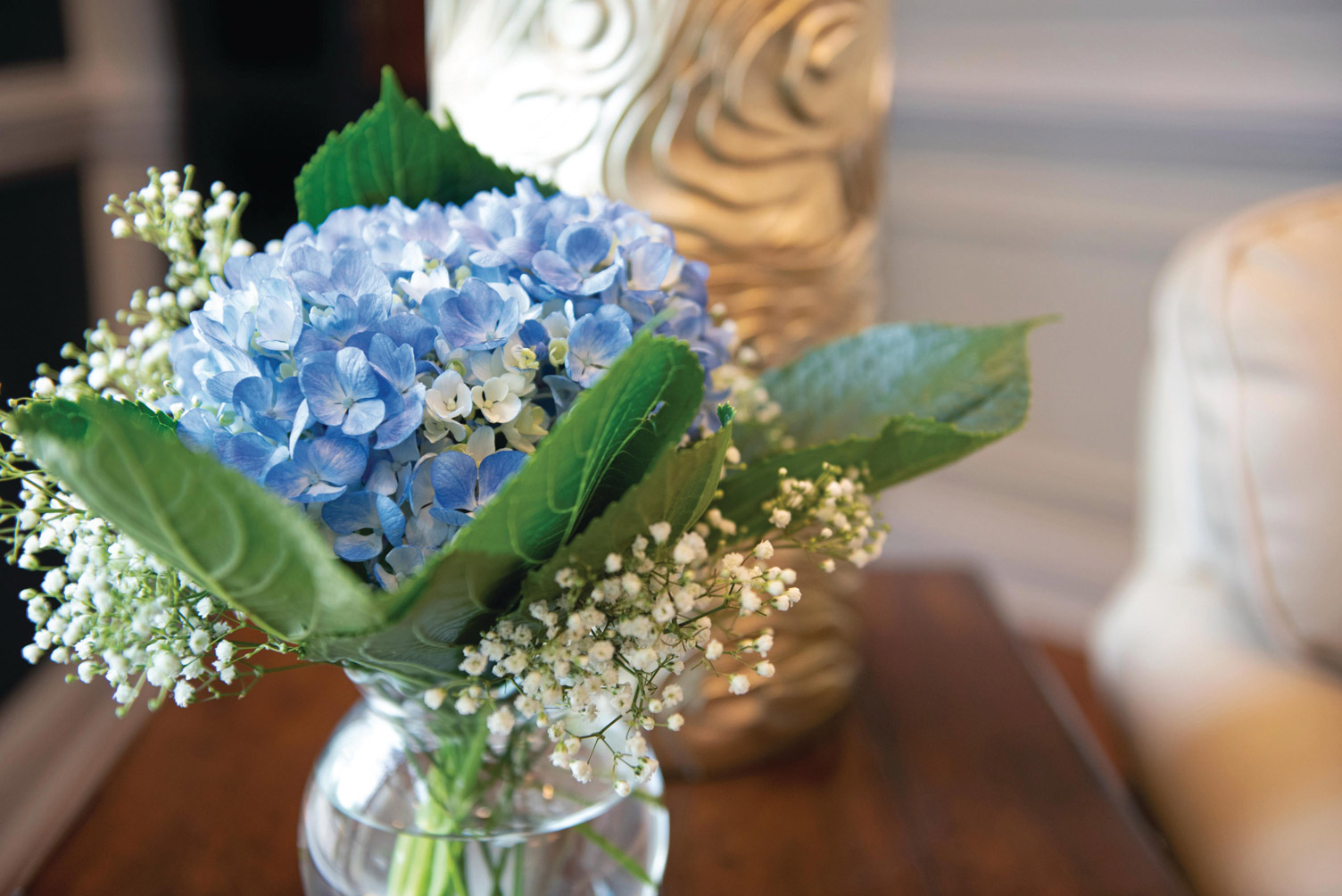 A glass vase with a blue and white floral. arrangement set atop a wooden table