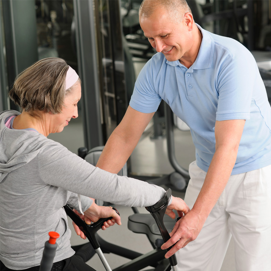 elderly woman on fitness machine being assisted by a team member