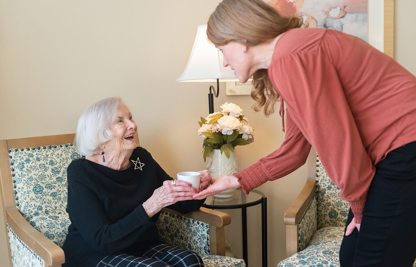 A naya caregiver helping a resident with coffee.