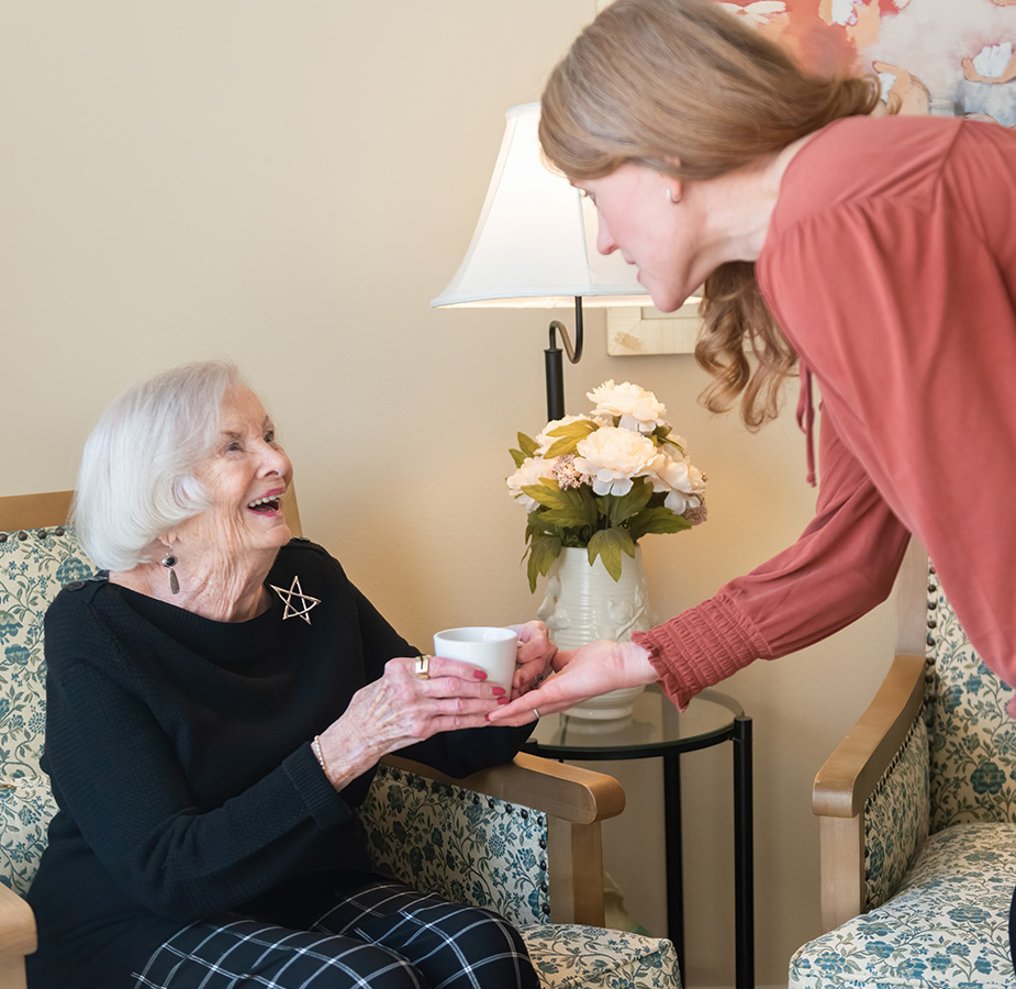 A person giving a cup of coffee to a resident.