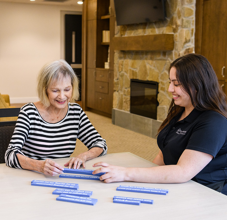 Caregiver works on a puzzle with a resident wearing a black and white striped shirt.