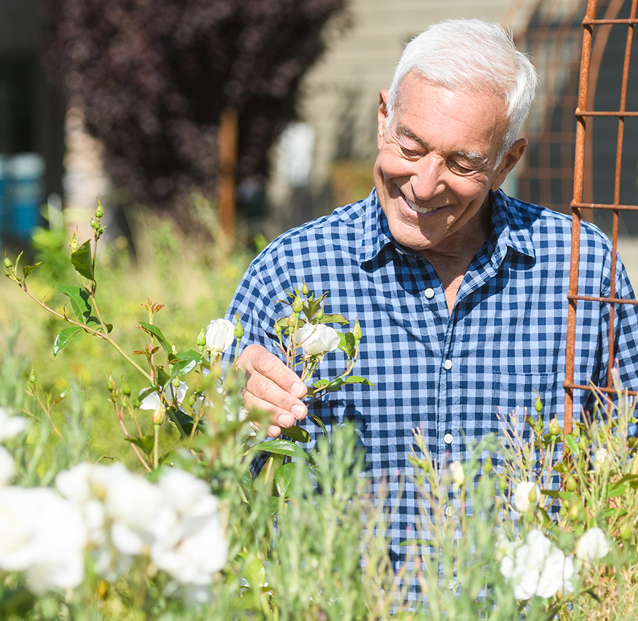 an elderly man is smiling at a flower outside
