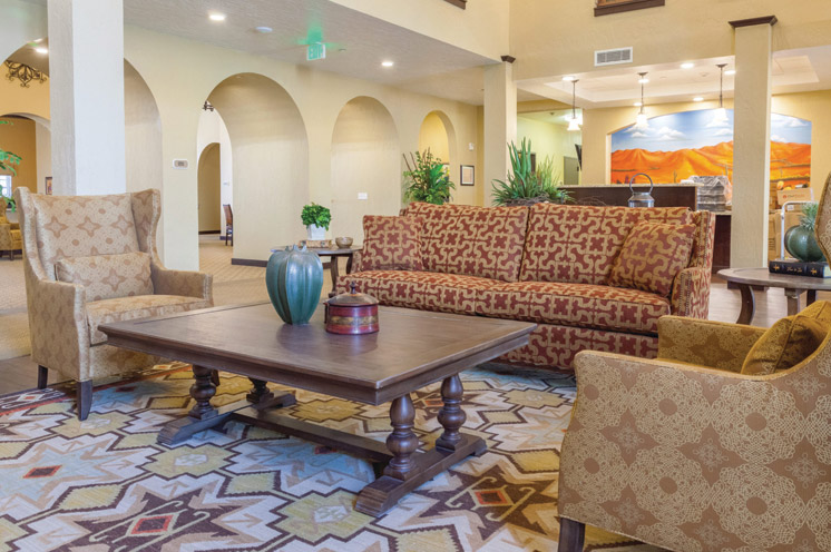 The Caliche Senior Living lobby, showing a retro armchair and couch with a painting of a classic Arizona landscape on the back wall.