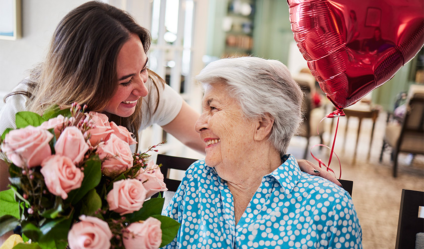 A woman is smiling at a resident who has a balloon and flowers.