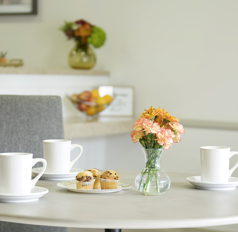 Coffee mugs on top of a white table with yellow flowers in a vase.
