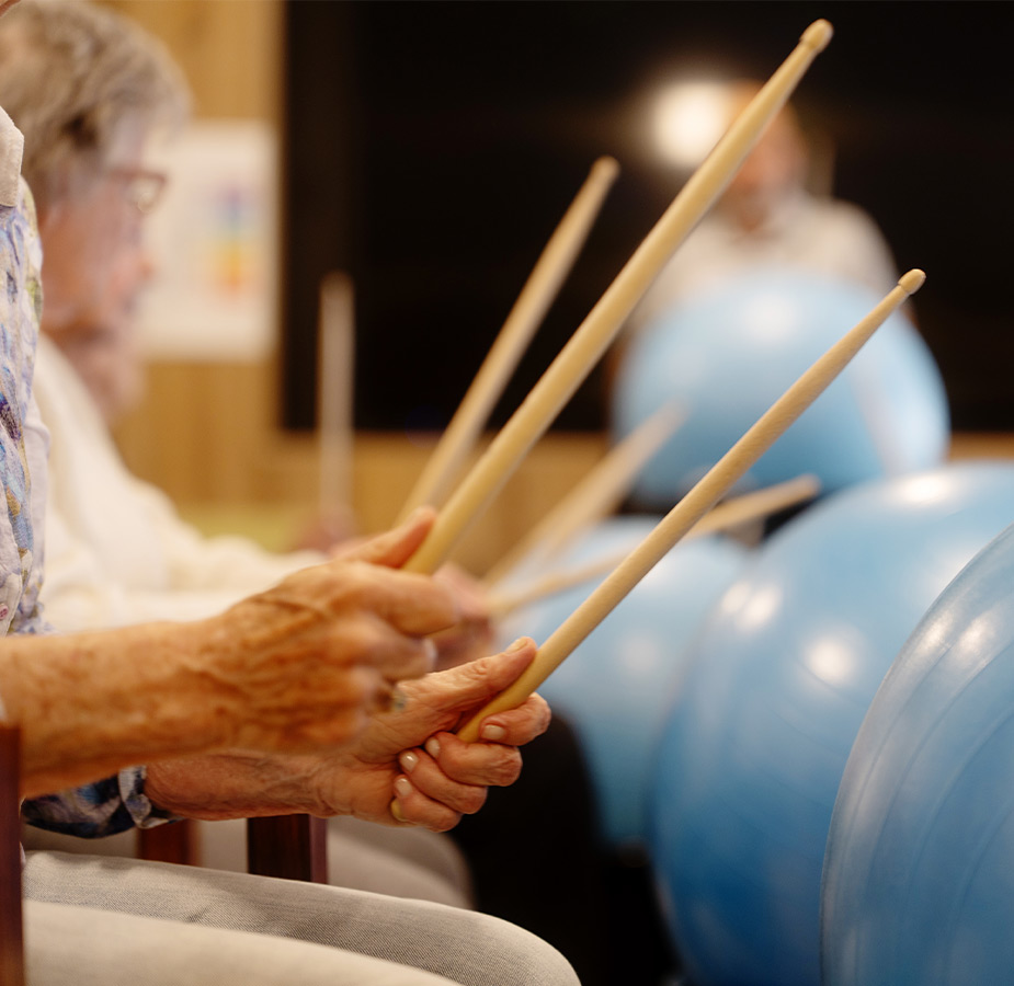 People with drum sticks hitting a blue ball.