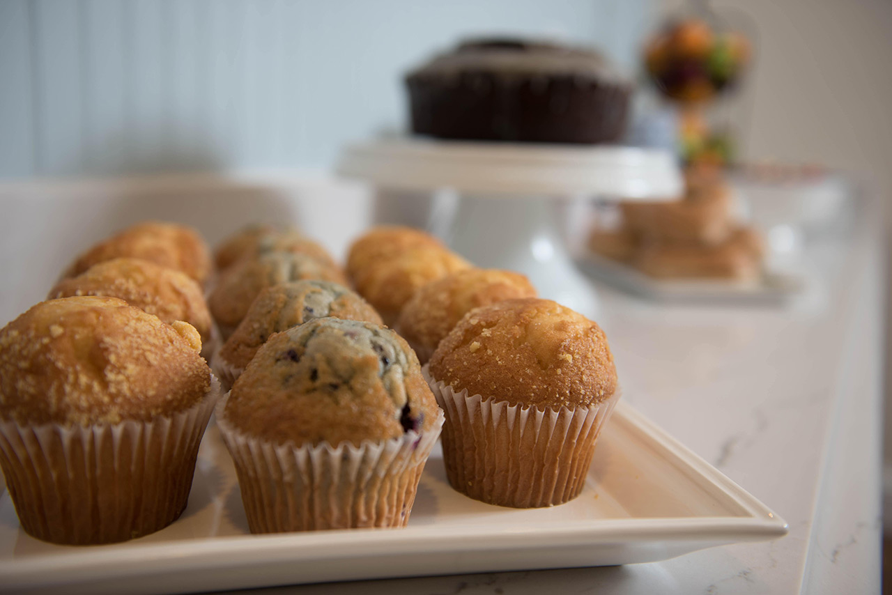 Tray of muffins with a cake behind them.