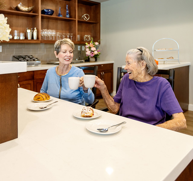 Two residents are having coffee and pastries at the breakfast bar.