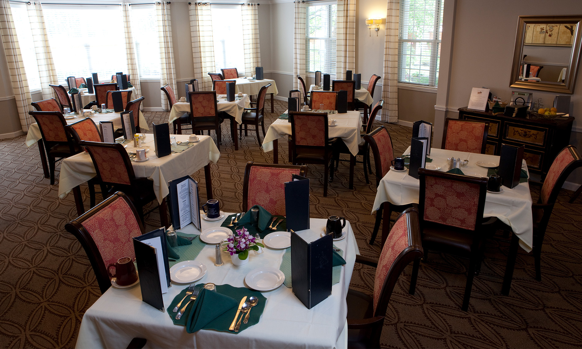 A formal dining room with white table cloths, menus, plates and flowers.
