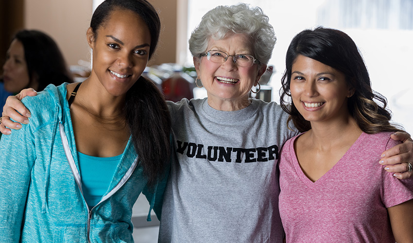 A senior woman with a volunteer shirt on with two younger girls.