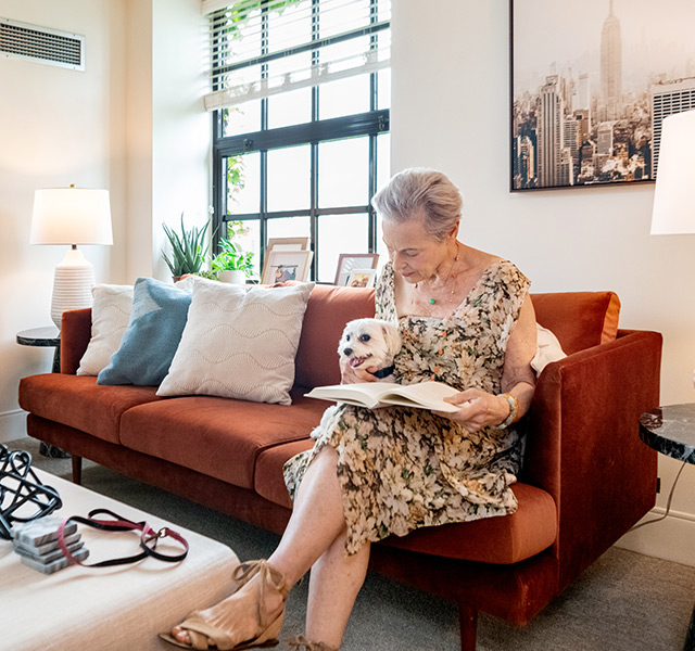 A resident sitting on the couch reading with dog.