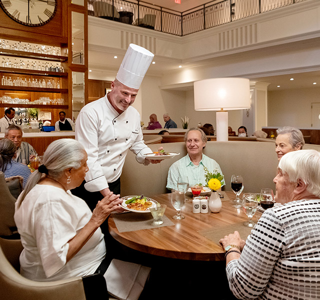 Residents eating in dinning room with chef at the table.