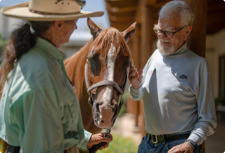 A resident petting a horse while talking to the stable attendant.