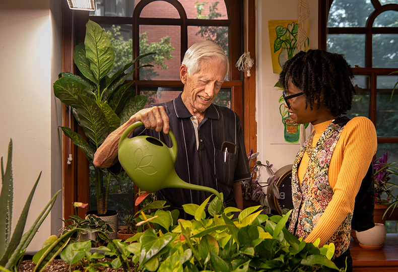 Elderly gentleman and his son standing in a field wearing skydiving gear Resident watering plants with an associate.