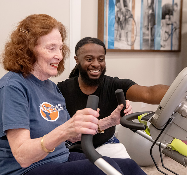 Associate helps resident on fitness equipment.