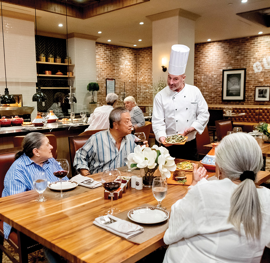 Group of people at a table with Chef visiting them.