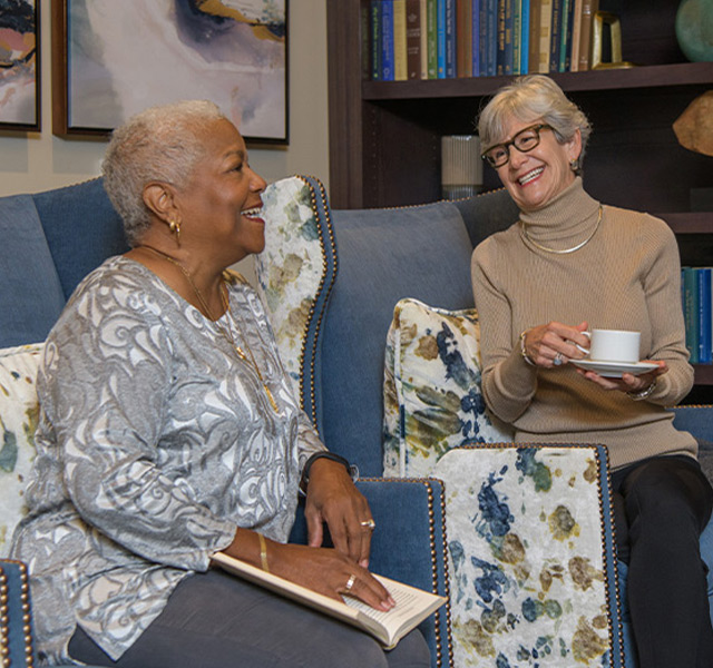 Women having fun sitting on a couch with coffee.