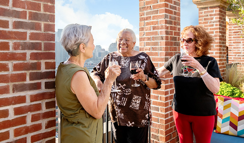 Three women enjoying drinks on the rooftop at happy hour.