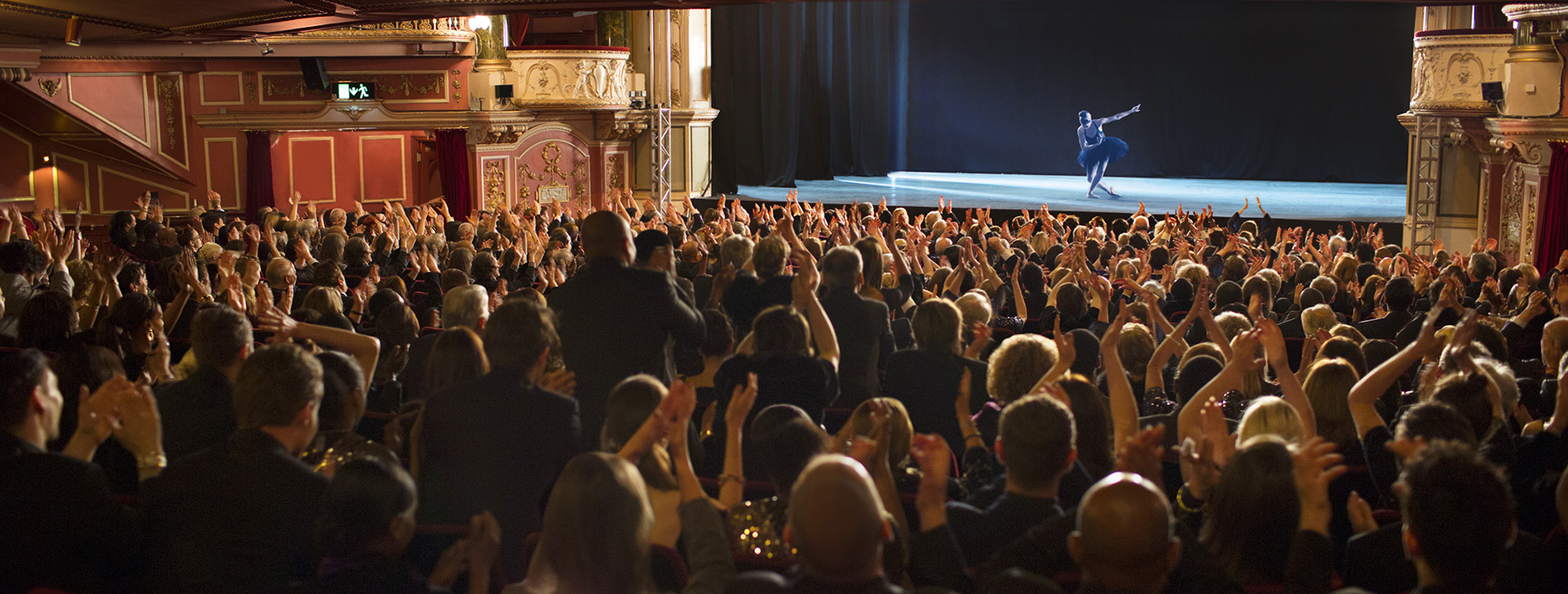 A stage with a ballet dancing bowing and a crowd full of people.