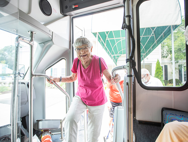 A resident in a pink shirt is smiling and entering a bus.