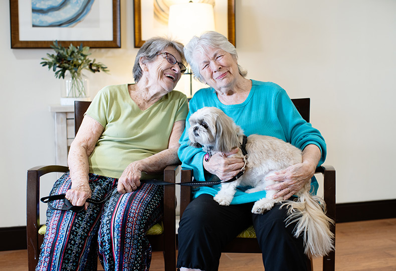 Two residents sitting down holding a dog.
