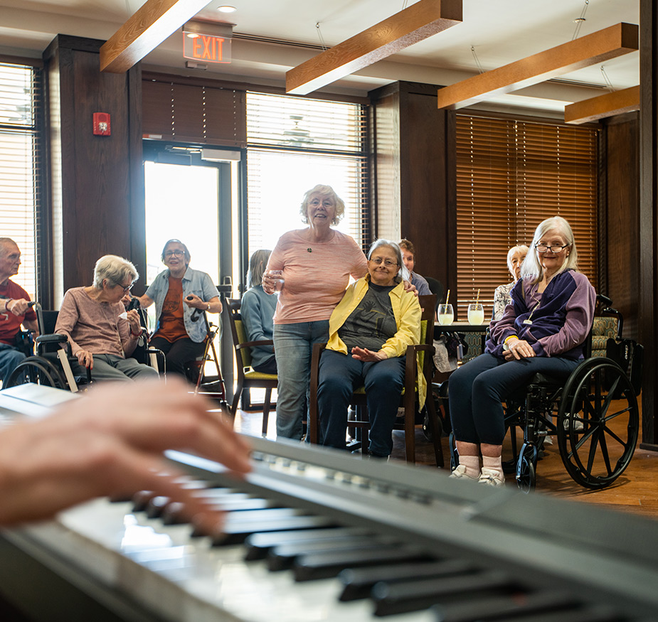 A person is playing piano while residents participate in a group activity.