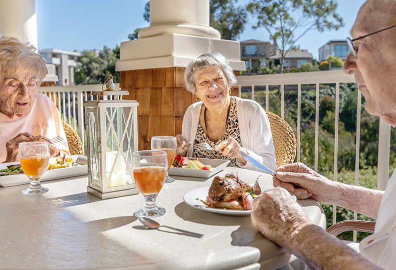 Three residents eating lunch outside on a patio.