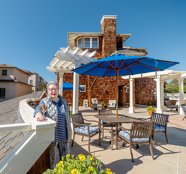 A resident standing outside on the sunny patio area with a glass of wine.