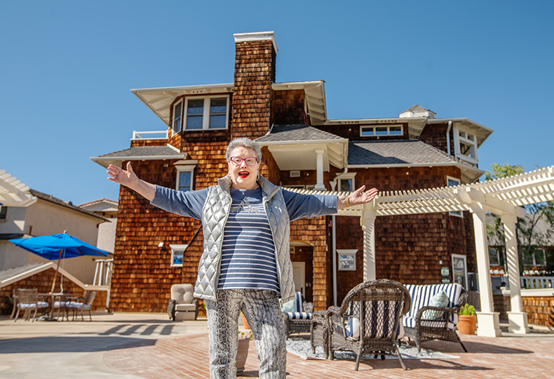 A resident standing outside on the sunny patio area with a glass of wine.