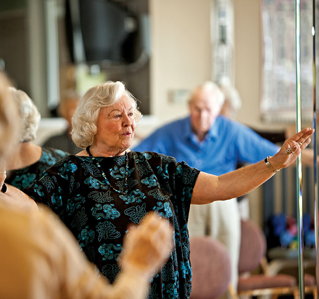 A resident is standing with their arms out on each side during a tai chi class.