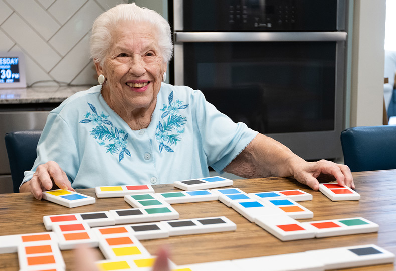 A resident is playing a game seated at a table in East Village Place.