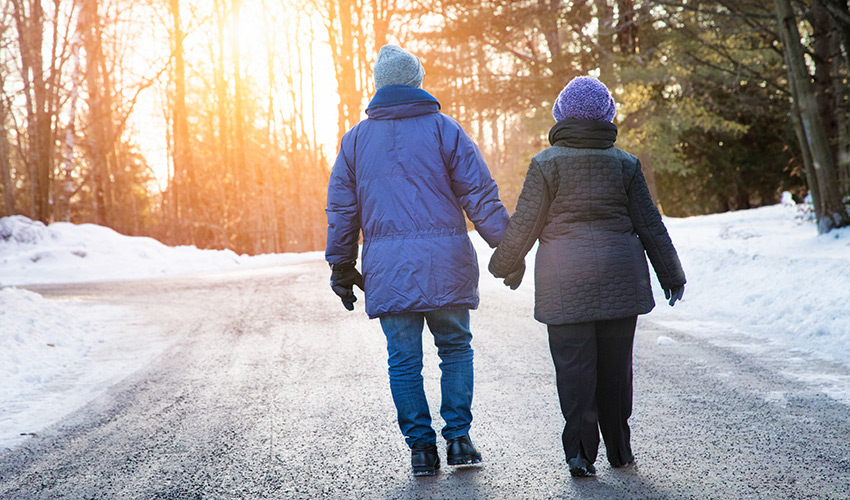 A senior couple holding hands walking in the winter sunset.