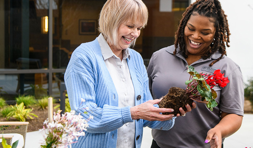 A watermark employee helping a resident at the garden bench.