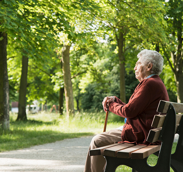 A resident with a cane sitting on a bench.