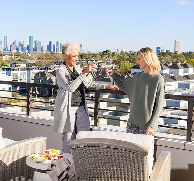 Two residents are standing outside on the rooftop patio enjoying glasses of wine.
