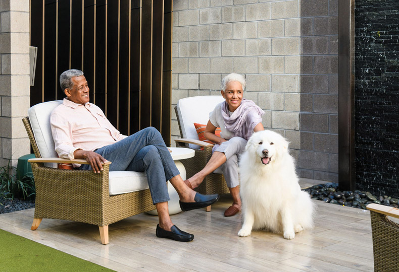 Two residents are sitting on the patio behind a large fluffy dog.