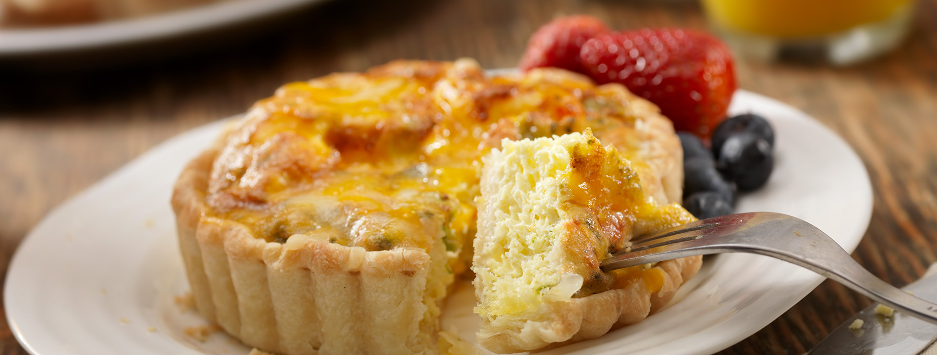 A mini quiche on a plate with fruit.