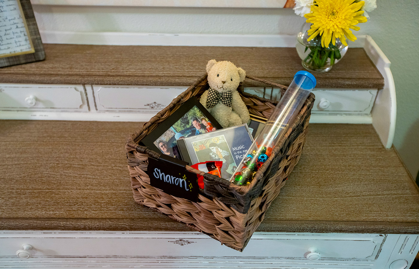 Basket with books and a teddy bear next to some flowers.