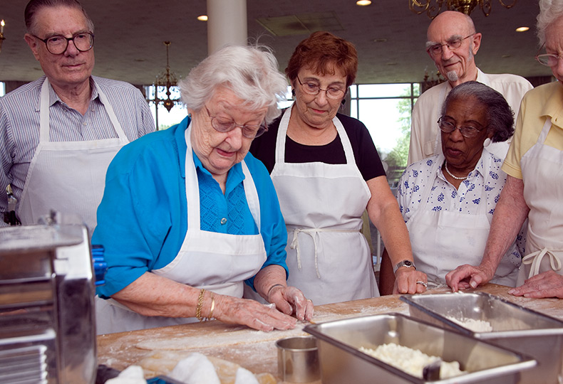Residents are observing a resident who is making pasta in a cooking class.