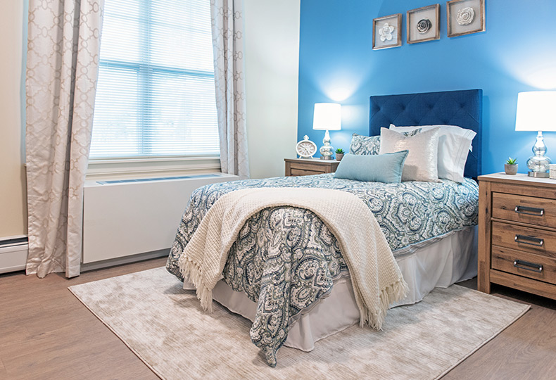 Furnished bedroom with bed, drawers, and soft lighting.