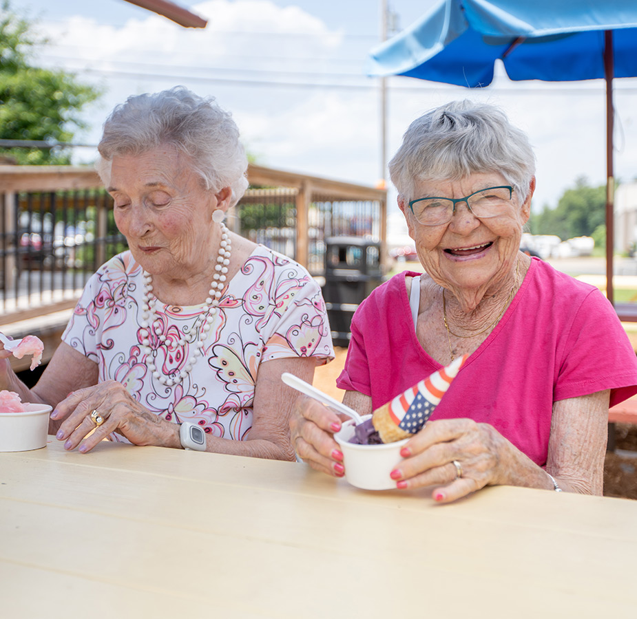 Two residents with ice cream are sitting outside at a table under an umbrella.