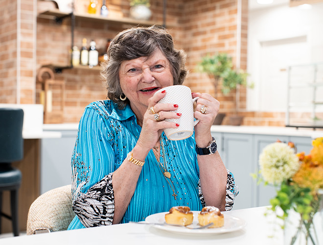 A resident is sitting at a table smiling and holding a cup of coffee.