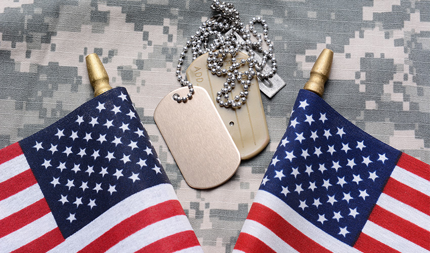 two small American flags and two dog tags on top of a military uniform