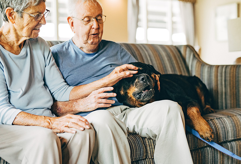Two residents are sitting on a sofa with their dog.