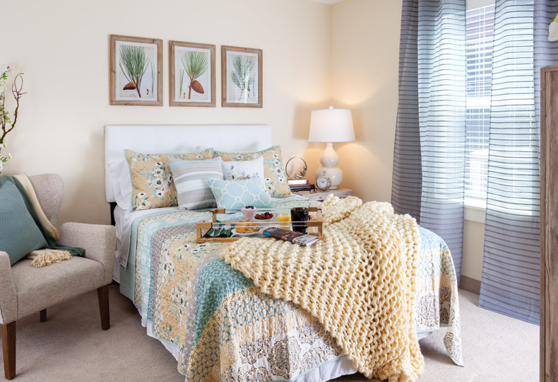 Furnished bedroom with chair, art on wall, and large window.
