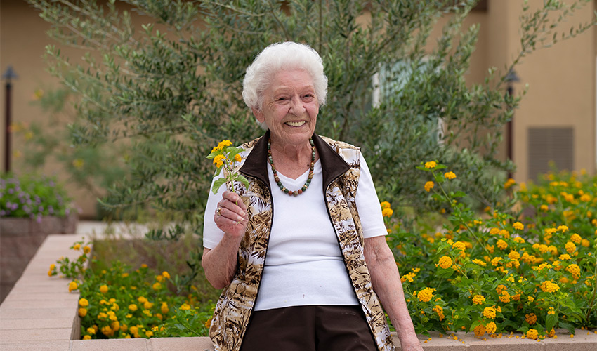 A person holding a flower and smiling outside.