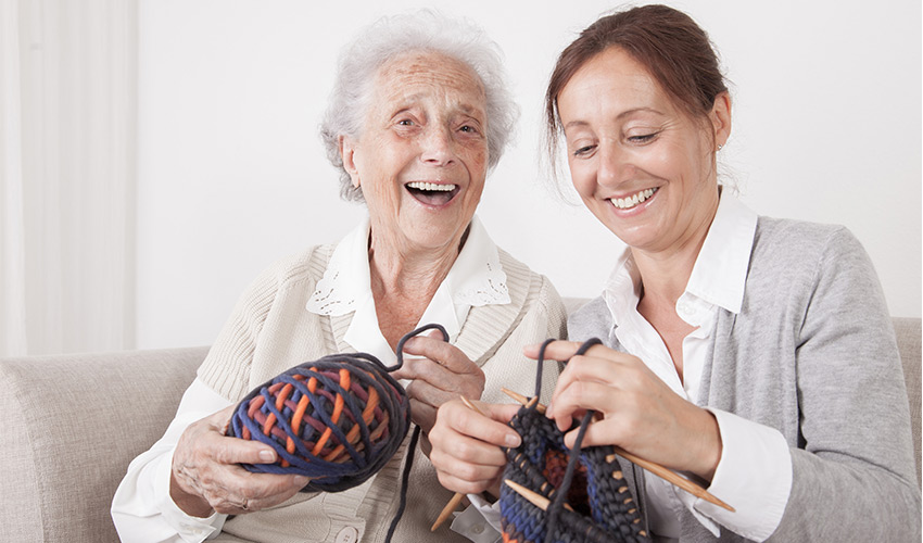 two people smiling while knitting
